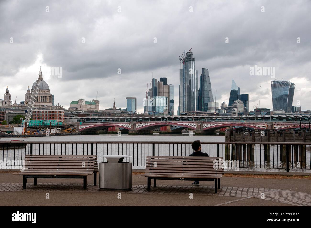 Uomo seduto su una panchina che guarda sul Blackfriars Bridge e, sullo sfondo, sui grattacieli del Financial Business. Londra, Inghilterra Foto Stock