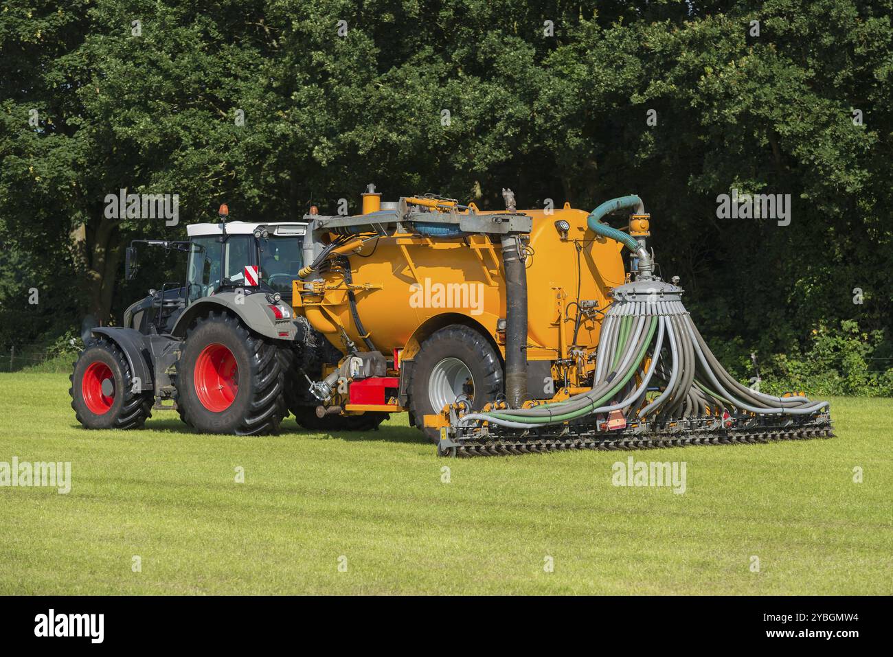 Iniezione di concime in un pascolo con un trattore verde e un carro armato giallo avvoltoio in estate Foto Stock