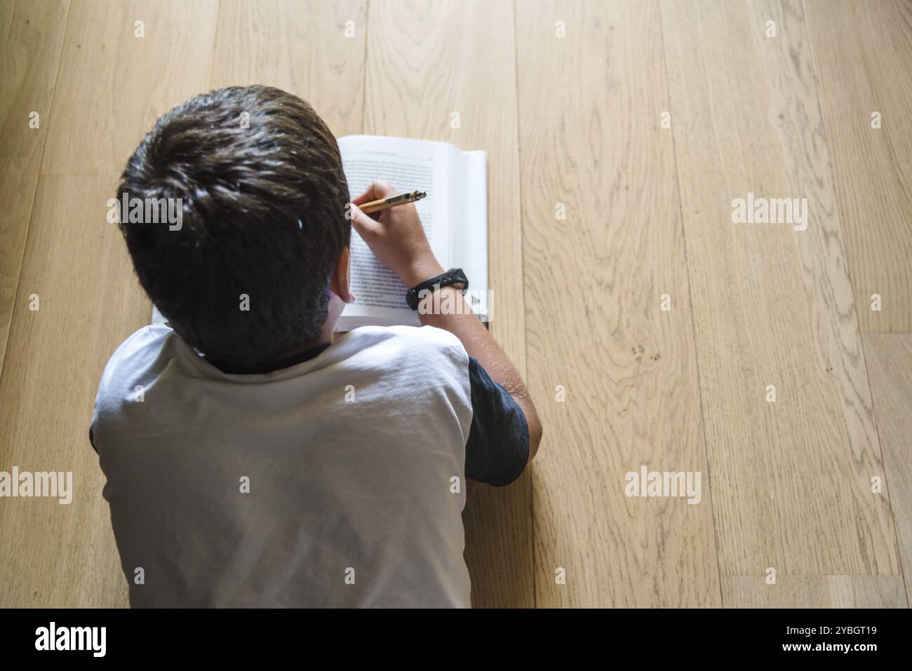 Little Boy bambino la lettura di un libro. Egli giace sul pavimento. Vista posteriore, il fuoco selettivo Foto Stock