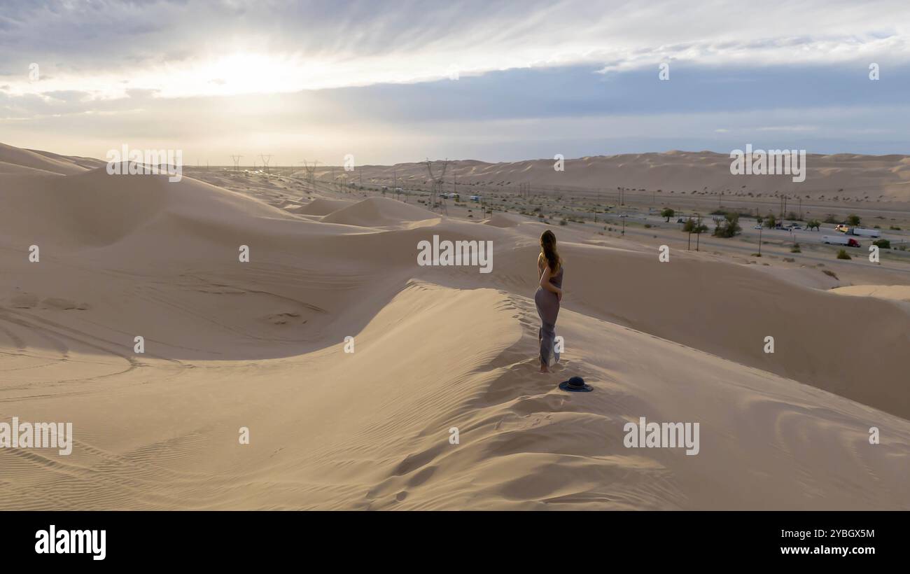 Il modello grazioso abbraccia la bellezza della natura tra le dune di sabbia, incarnando l'eleganza sullo sfondo di un vasto e naturale splendore Foto Stock