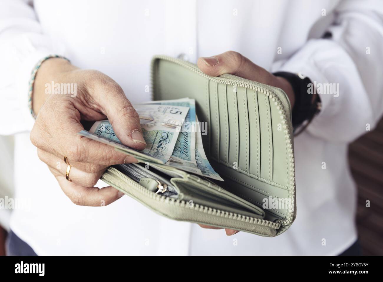 Stretta di mano di donna tenendo fuori di sterline dalla sua borsa Foto Stock