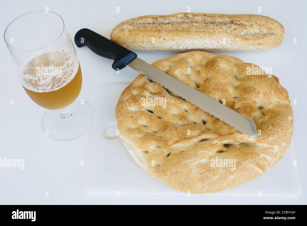 Filone di pane, la birra e il coltello sul tavolo bianco, cibo closeup. Vista superiore Foto Stock