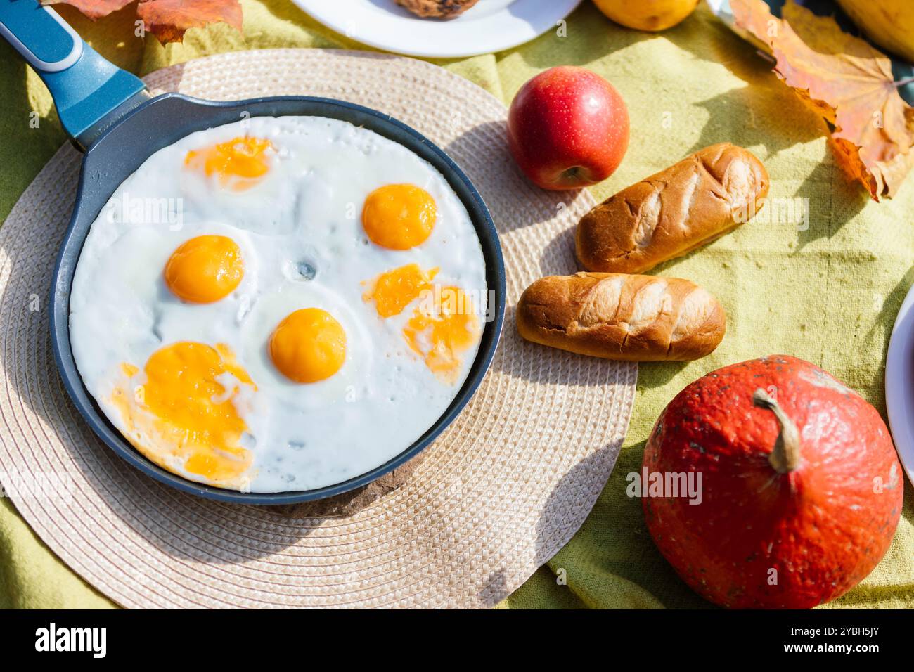 Riuniti su una colorata coperta da picnic, una deliziosa colazione include uova fritte con tuorli luminosi, mele fresche e pane soffice al forno, per creare un ingresso Foto Stock