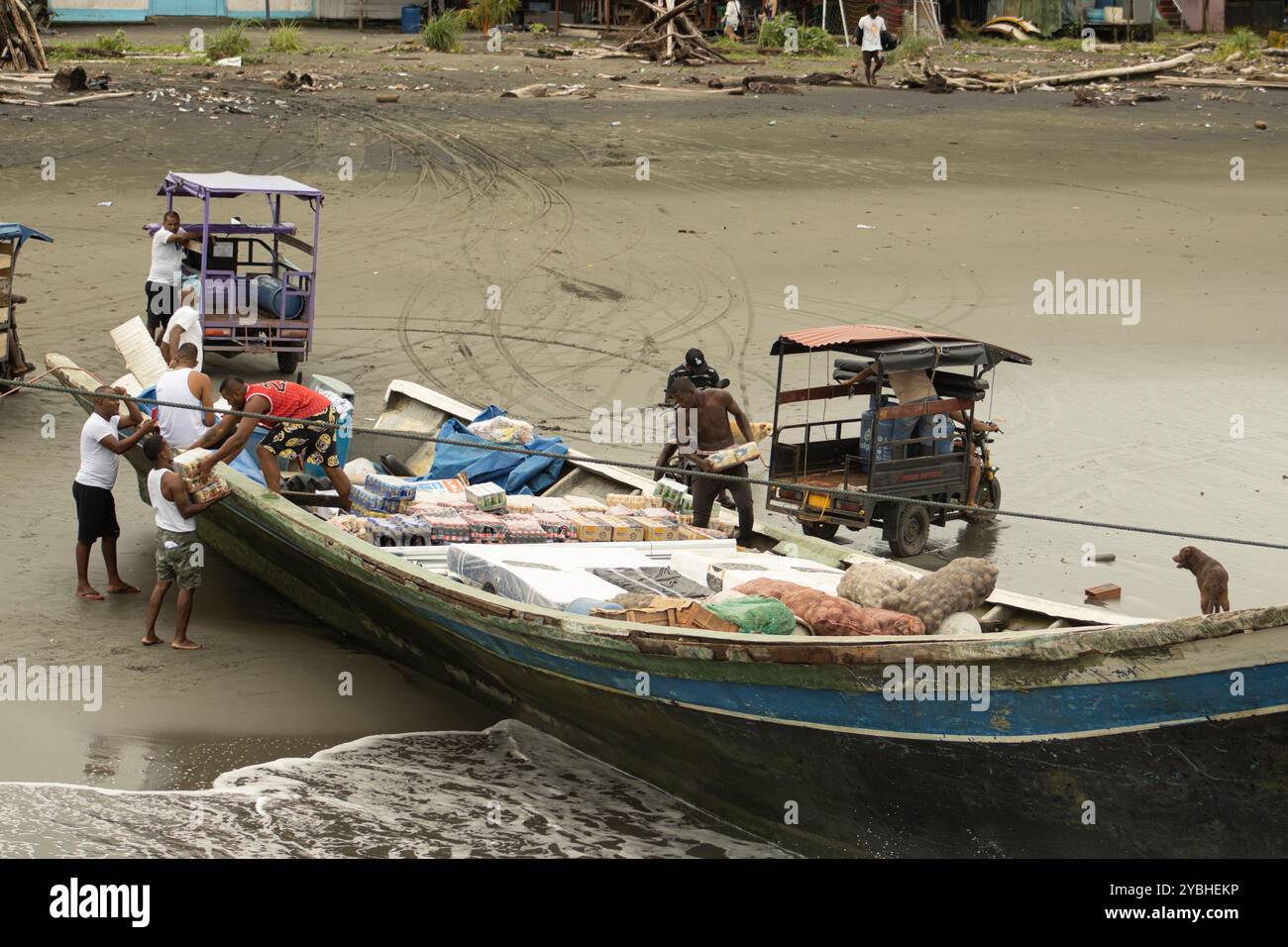 Gli uomini scaricano rifornimenti da una barca sulla spiaggia sabbiosa di Bahía Málaga, Colombia. I beni vengono trasferiti a un piccolo veicolo per la distribuzione nell'entroterra. Foto Stock