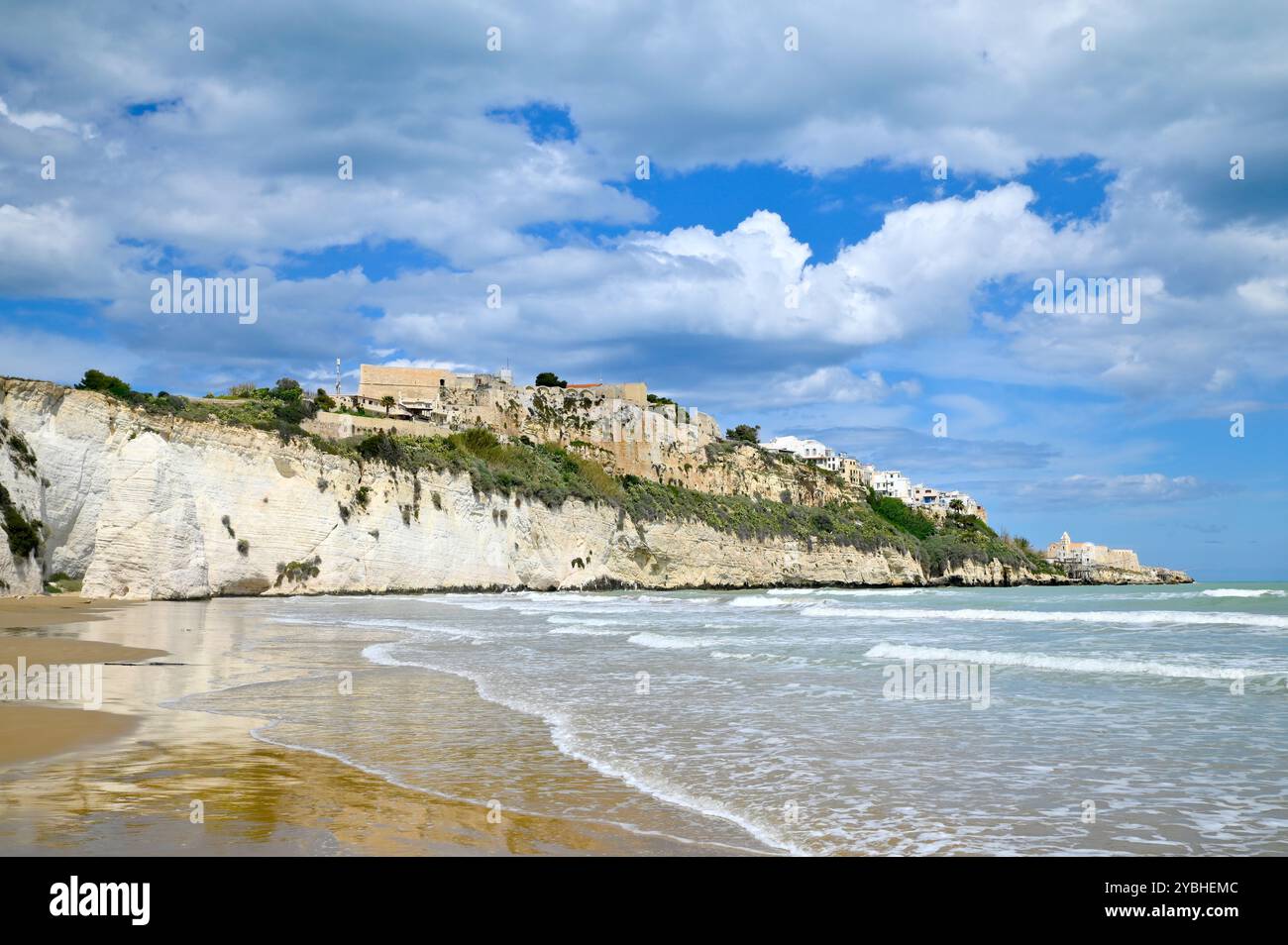 Vista sulla baia e Pizzomunno vicino a Vieste con il paese di Vieste arroccato sulla roccia e le onde del mare in primo piano Foto Stock