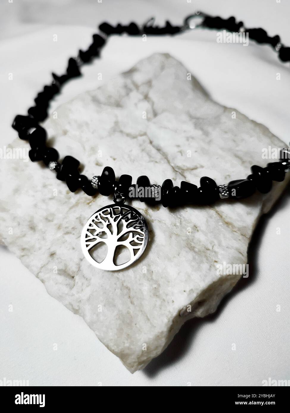 Collana di pietre preziose in agata nera con il fascino dell'albero della vita su sfondo bianco. Accessorio femminile, moda femminile. Gioielli in pietra naturale con paillettes piatte, perline - Immagine stock catturata con smartphone