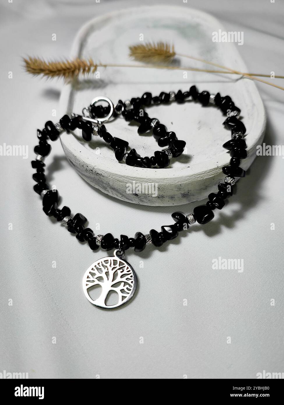 Collana di pietre preziose in agata nera con il fascino dell'albero della vita su sfondo bianco. Accessorio femminile, moda femminile. Gioielli in pietra naturale con paillettes piatte, perline - Immagine stock catturata con smartphone