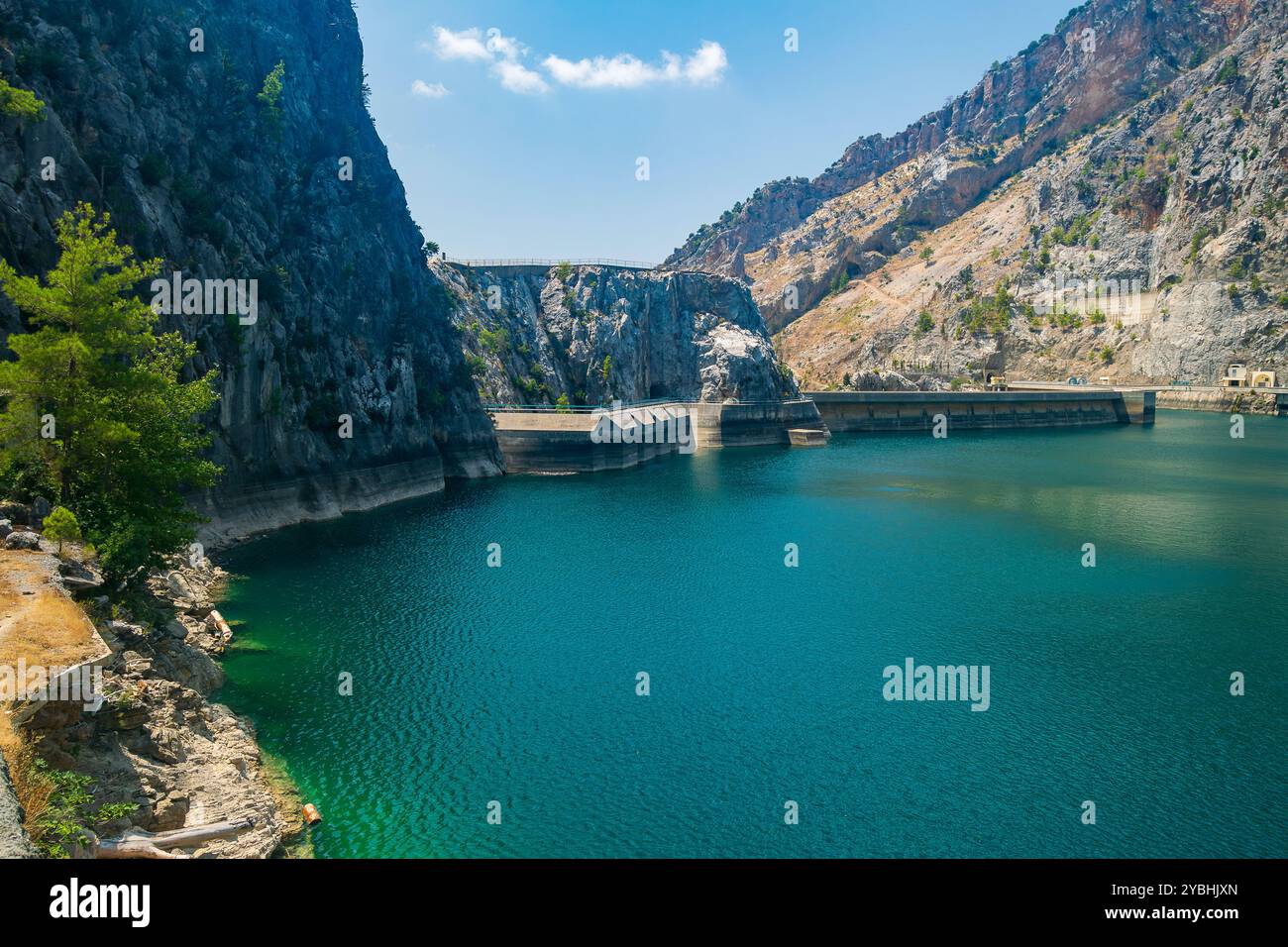 Vista panoramica della diga di Oymapinar in lontananza contro un cielo blu e un bacino idrico verde in primo piano in una soleggiata giornata estiva Foto Stock
