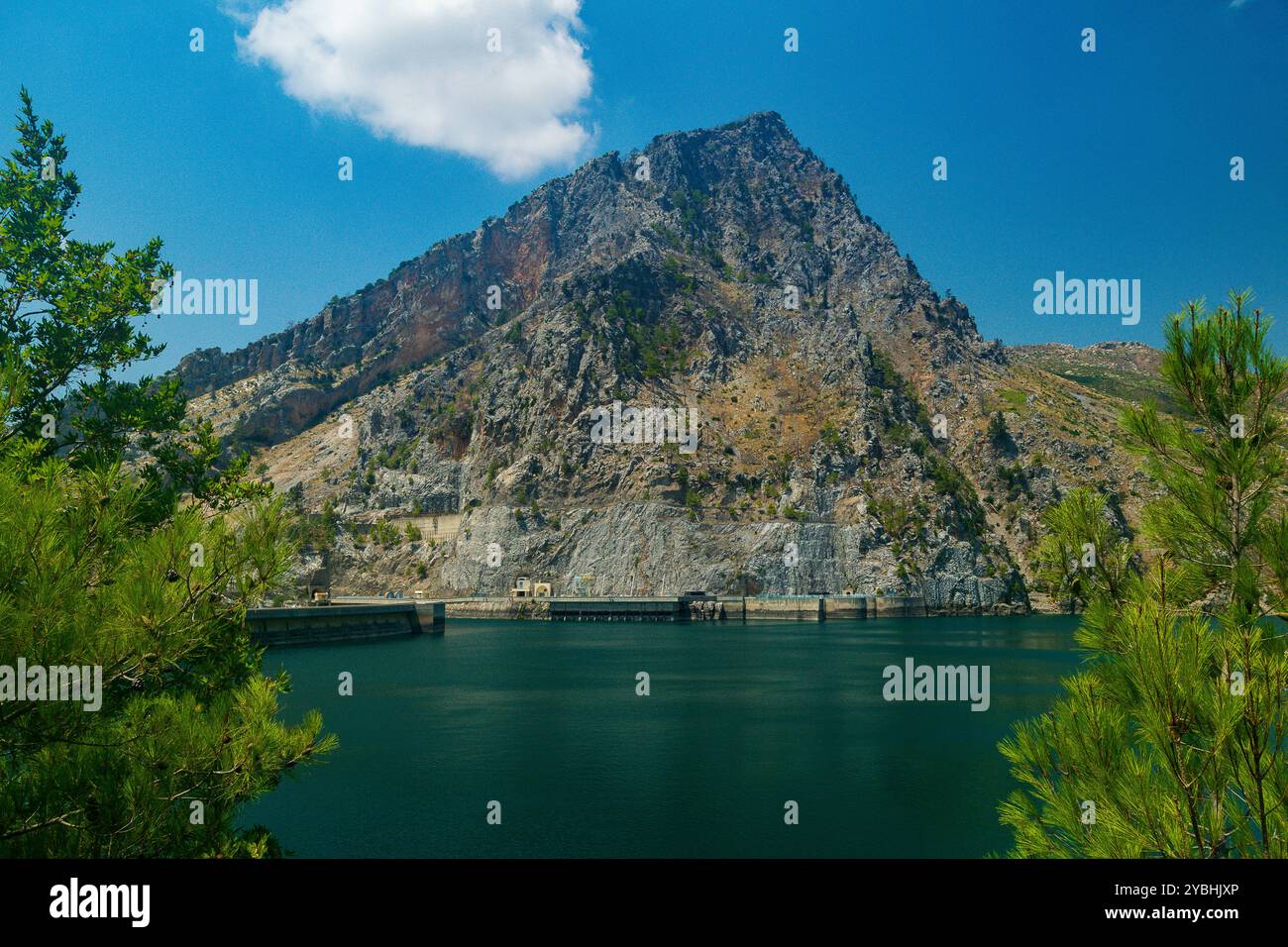 Vista panoramica della diga di Oymapinar in lontananza contro un cielo blu e un bacino idrico verde in primo piano in una soleggiata giornata estiva Foto Stock