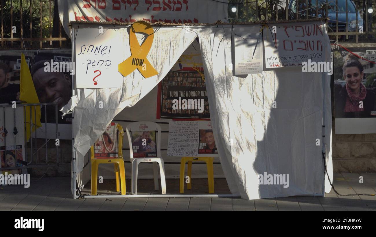 GERUSALEMME - 18 OTTOBRE: Una tradizionale capanna temporanea sukkah, costruita per essere utilizzata durante la festa ebraica di Sukkoth con un cartello a forma di nastro giallo che simboleggia la speranza e la simpatia per le famiglie degli ostaggi, si trova accanto alla tenda delle famiglie degli ostaggi fuori dalla residenza del primo ministro, in mezzo alla guerra a Gaza e all'escalation di Hezbollah, il 18 ottobre 2024 a Gerusalemme. Israele Foto Stock