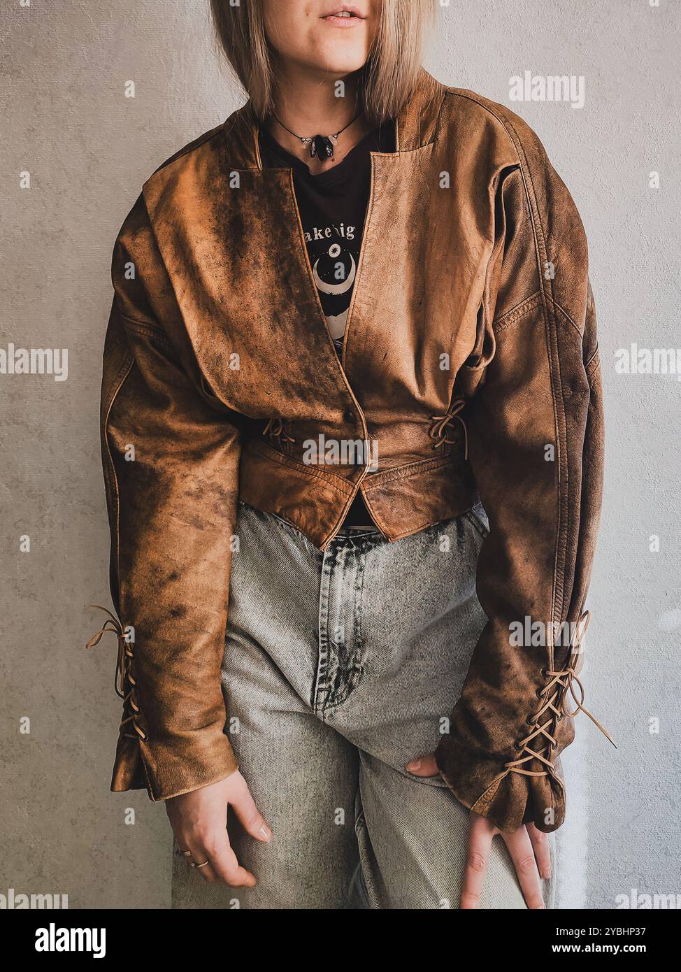 Giacca in pelle marrone vintage sul retro di una donna dai capelli biondi, giacca grunge corta, bolero da donna in similpelle, giacca in pelle con lacci anni '80 anni '90, abiti da donna vintage, outfit retrò - Immagine stock catturata con smartphone