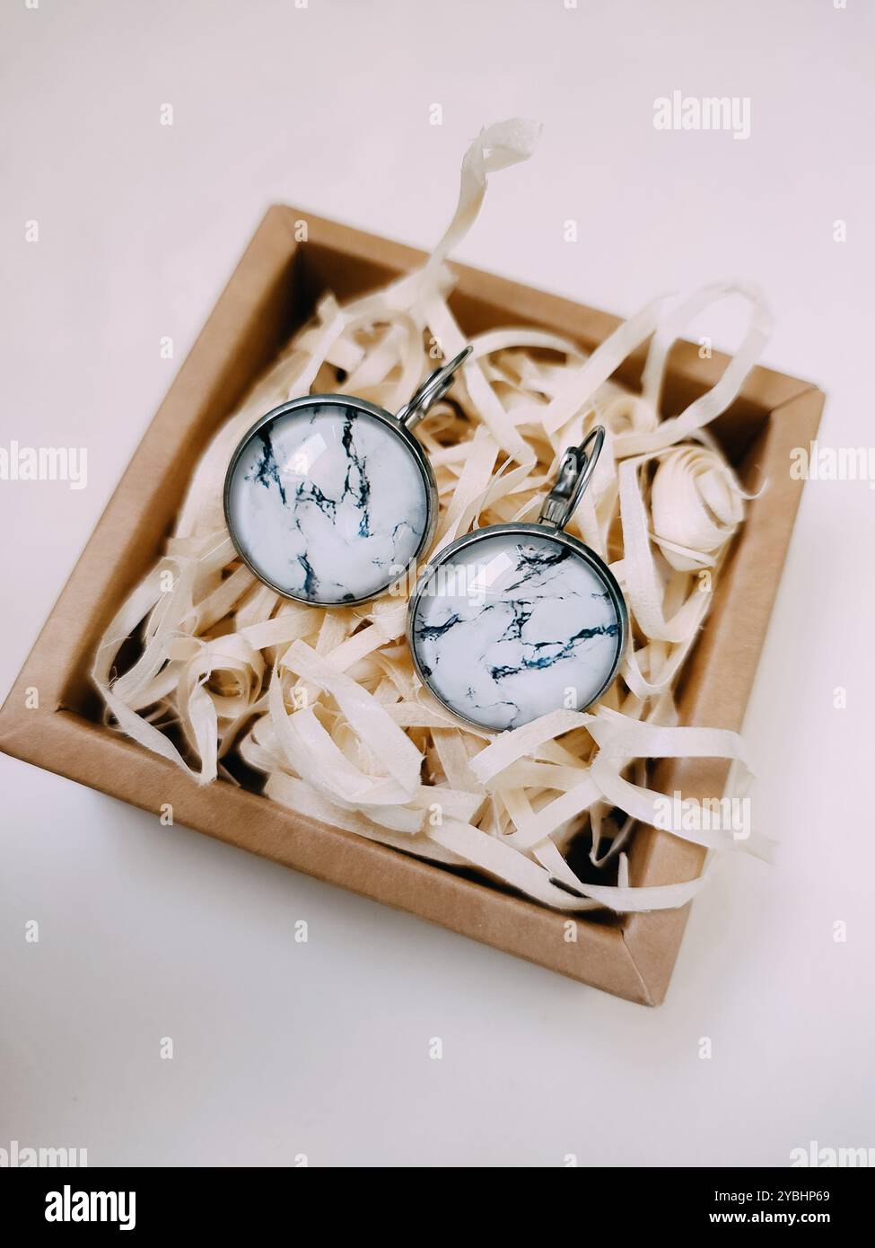 Orecchini in pietra rotondi in resina realizzati a mano in piccola scatola di gioielli in carta artigianale con riempimento per pacchi. accessori e gioielli in argento ispirati alla natura Foto Stock