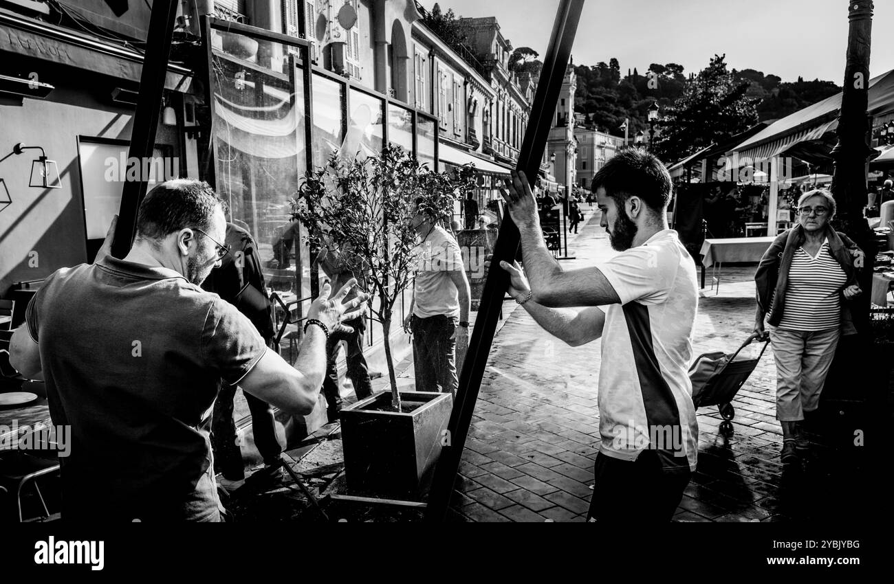 Due uomini che erigono una pausa vento in un caffè nel mercato della frutta e dei fiori a Cours Saleya, Nizza, Francia Foto Stock