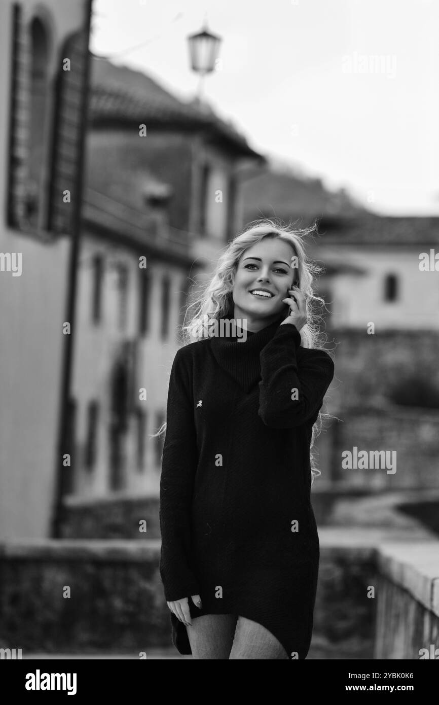 Una giovane donna sorride mentre cammina e parla al telefono in una storica città europea. Si sta godendo i suoi viaggi all'estero Foto Stock