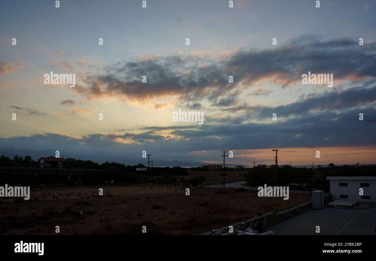 Mentre il sole scende sotto l'orizzonte, le calde sfumature di arancione e viola si intrecciano tra le nuvole, creando un'atmosfera serena sulla tranquilla valle a t Foto Stock