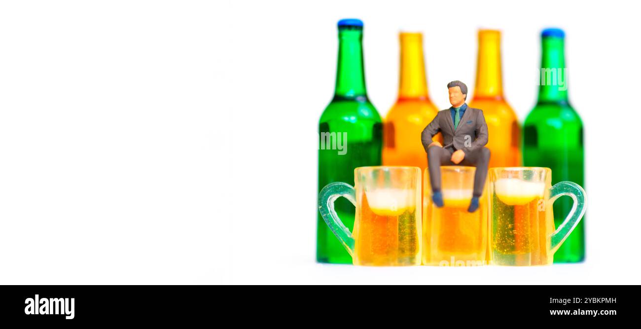 Rappresentazione umoristica di un uomo d'affari in miniatura seduto su tazze da birra con bottiglie colorate sullo sfondo isolate sul bianco con spazio per le copie. Foto Stock