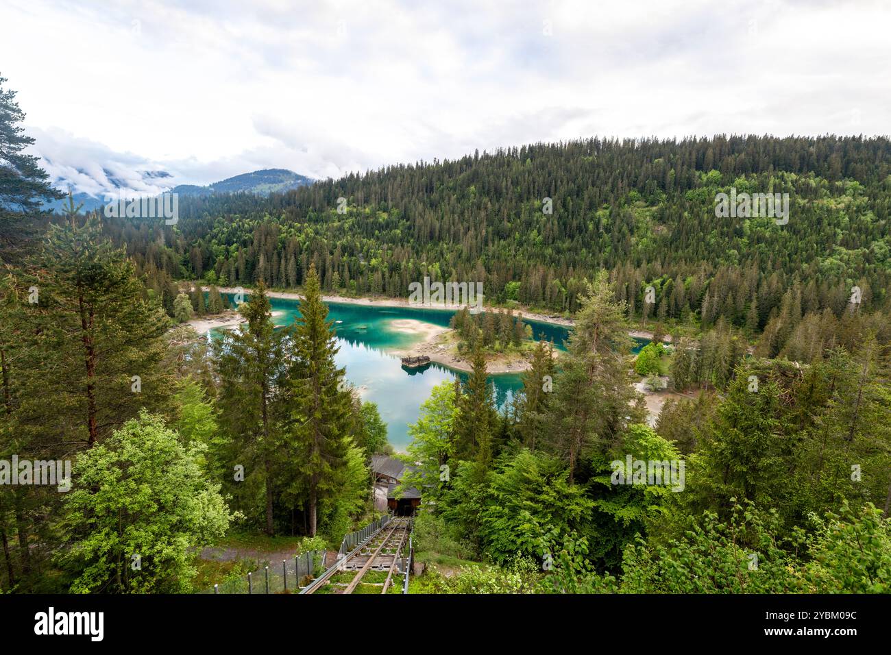 Linea di tram di montagna che scende verso un lago ghiacciato circondato dalla foresta Foto Stock