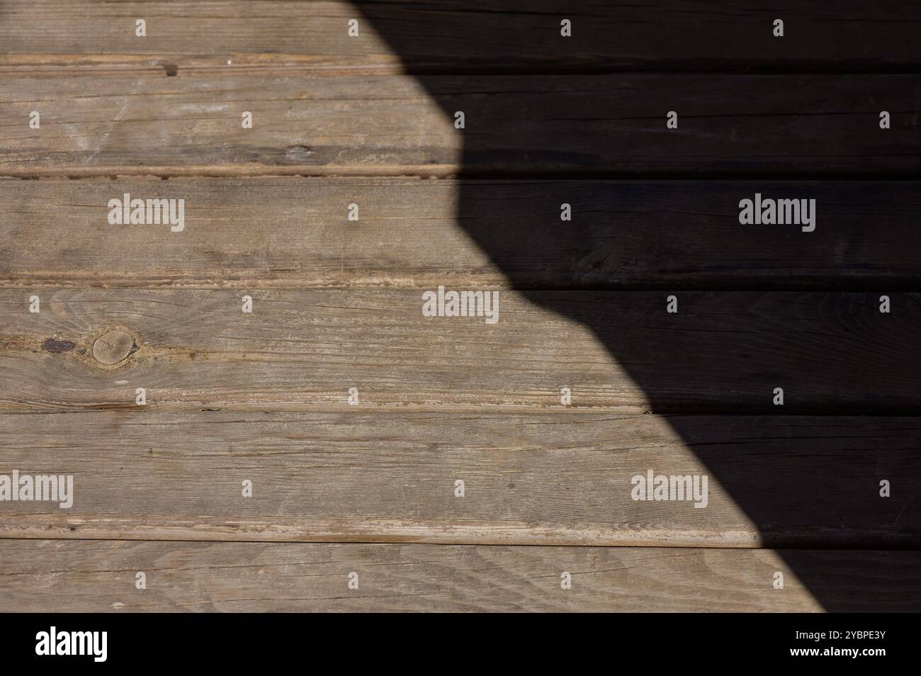 La luce del sole filtra su un ponte in legno rustico, creando un bellissimo contrasto tra luce e ombra. Tavole piene di tempo raccontano storie di tempo e di elemen Foto Stock