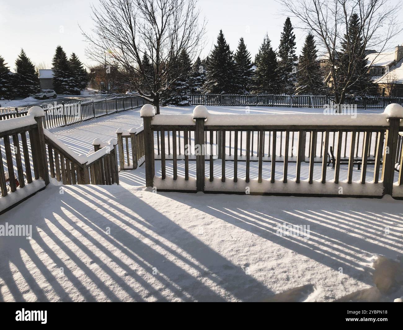 Il sole del tardo pomeriggio getta lunghe ombre sulla neve bianca fresca accumulata sulle ringhiere e sui paletti di un ponte sul cortile all'inizio dell'inverno. Foto Stock