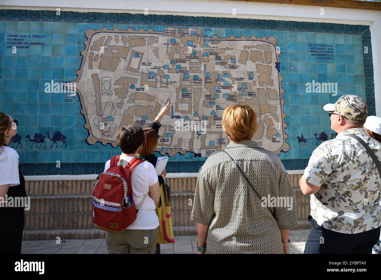 Khiva, Uzbekistan - 15 settembre 2024: Un gruppo di turisti ascolta una guida turistica vicino alla mappa del centro storico di Khiva sulle piastrelle di ceramica Foto Stock