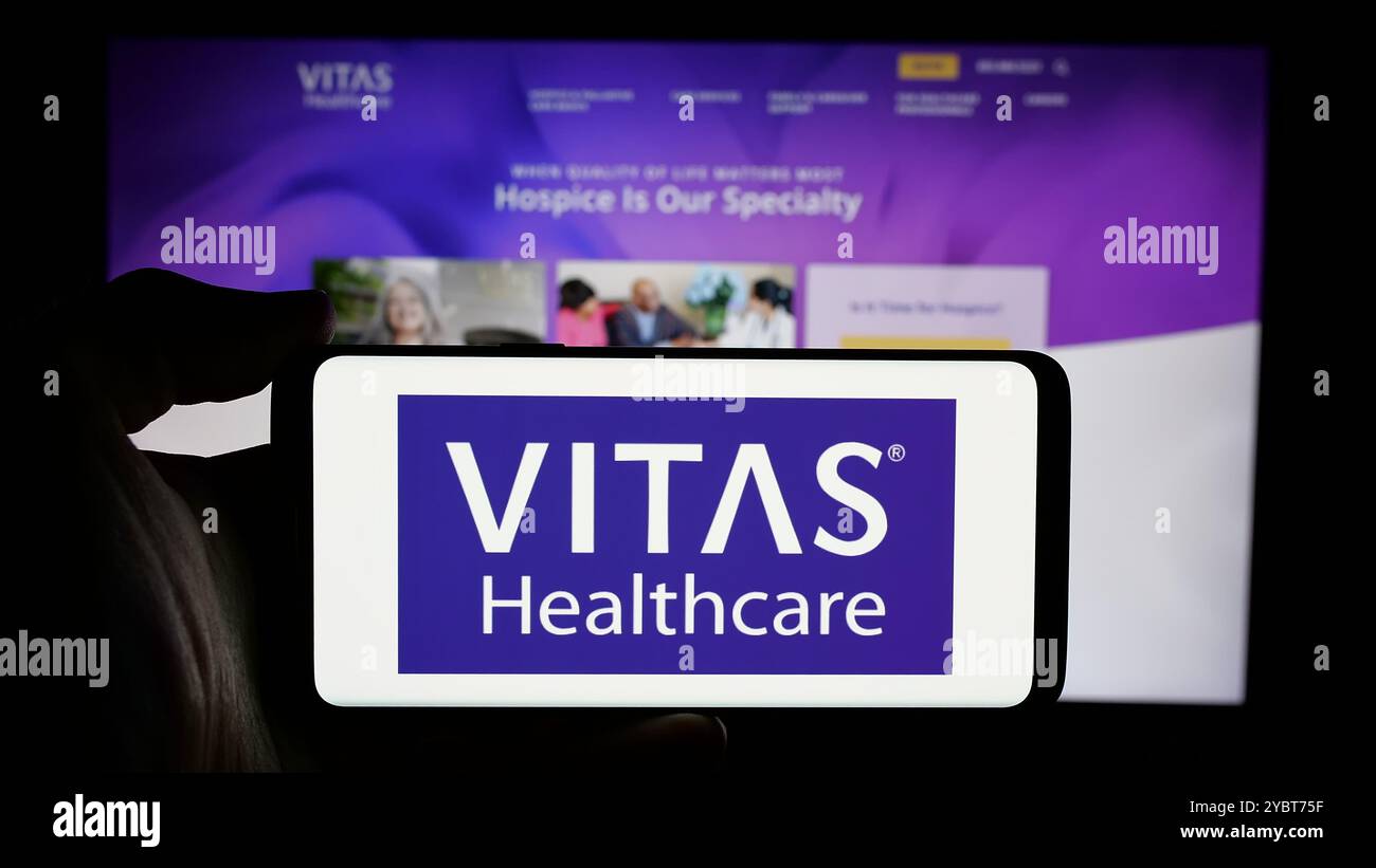 Persona che tiene il cellulare con il logo della società sanitaria degli Stati Uniti VITAS Healthcare sullo schermo di fronte alla pagina web aziendale. Mettere a fuoco il display del telefono. Foto Stock