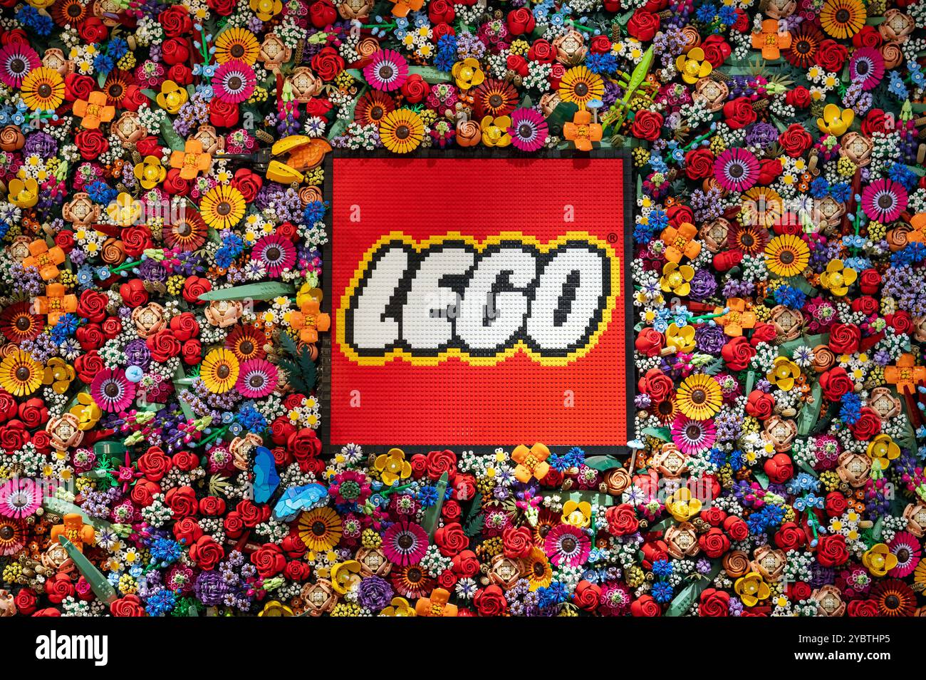 Il logo lego realizzato con mattoni di plastica, circondato da fiori colorati anch'essi realizzati con mattoni Foto Stock