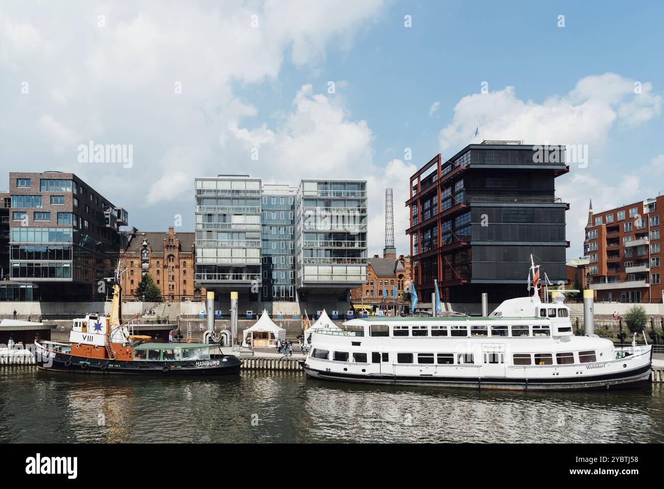 Amburgo, Germania, 7 agosto 2019: Paesaggio urbano del canale Sandtorhafen con navi ormeggiate sul porto e edifici residenziali moderni di lusso. Giornata di sole Foto Stock