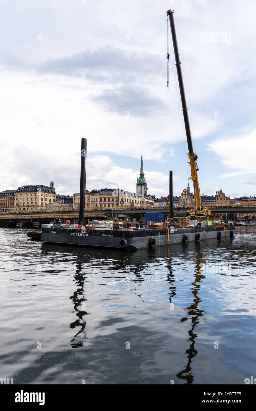 Stoccolma, Svezia, 8 agosto 2019: Chiatta galleggiante da costruzione con una gru sul porto contro il paesaggio urbano di Gamla Stan a Stoccolma, in Europa Foto Stock