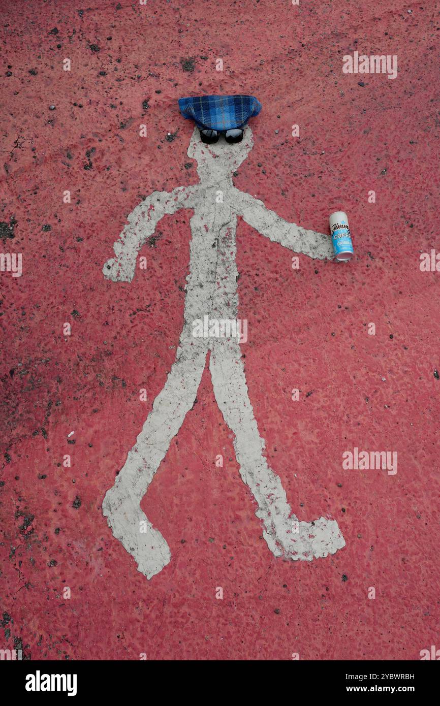 Uomo dipinto su asfalto rosso, con un cappello Harris Tweed, occhiali da sole e lattina di caffè freddo Foto Stock