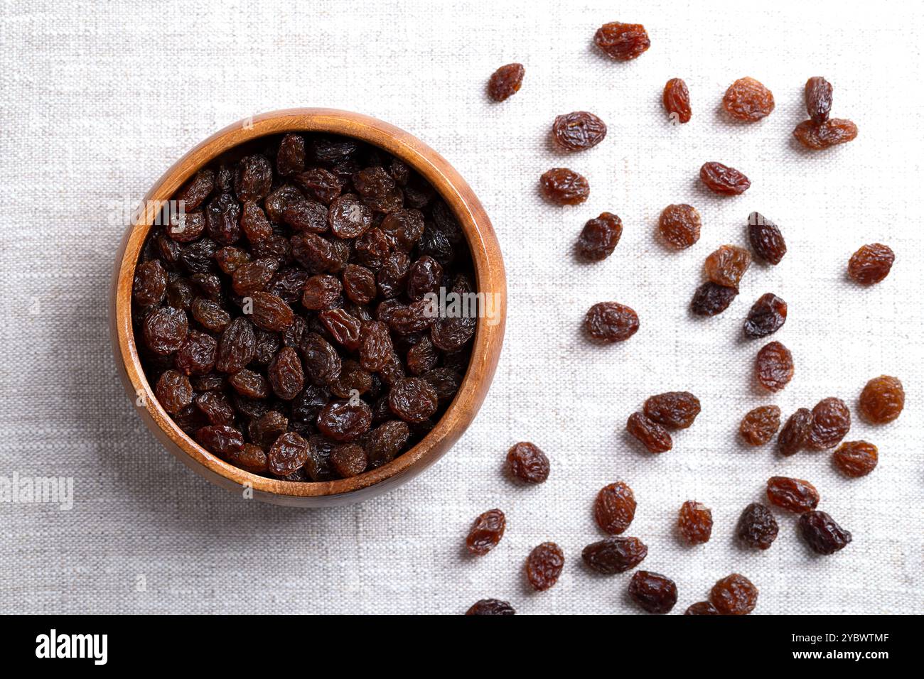 Uvetta commerciale comune, in una ciotola di legno su tessuto di lino. Uvetta da uva passa secca di colore scuro, da consumare cruda o da utilizzare in cucina. Foto Stock