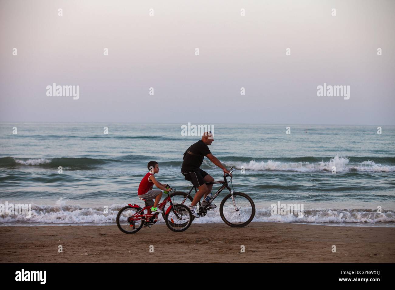 Padre e figlio si godranno il momento di andare in bicicletta vicino al mare. Foto Stock