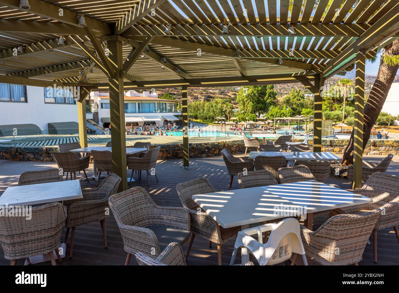 Sedie e tavoli in vimini sulla terrazza esterna sotto il pergolato vicino alla piscina con vista sulle montagne. Creta. Grecia. Foto Stock