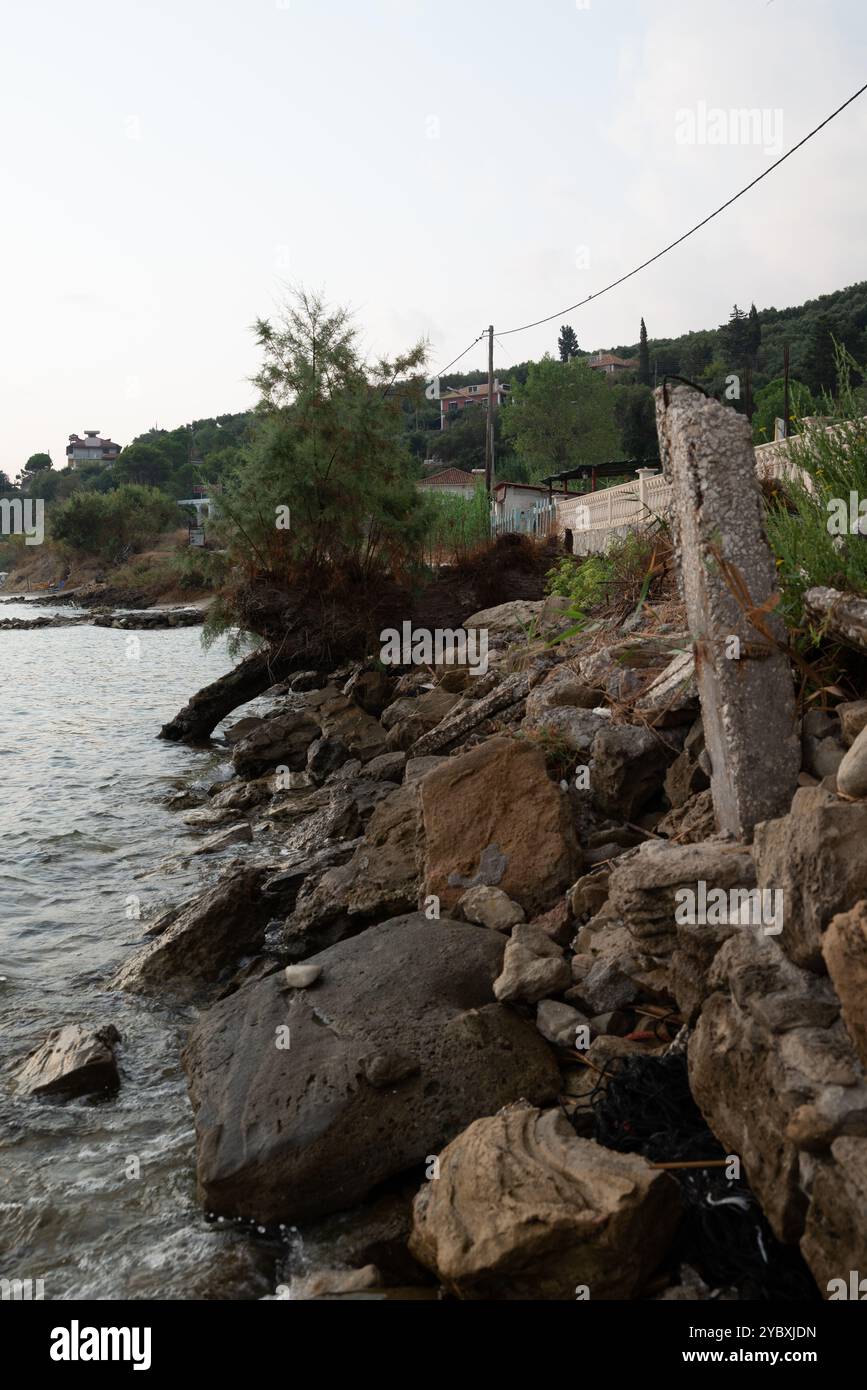 L'erosione costiera ha un pesante impatto sulle strutture e sulla vegetazione. Questa scena mostra i danni a una proprietà sul mare. Vediamo rocce e un albero caduto Foto Stock