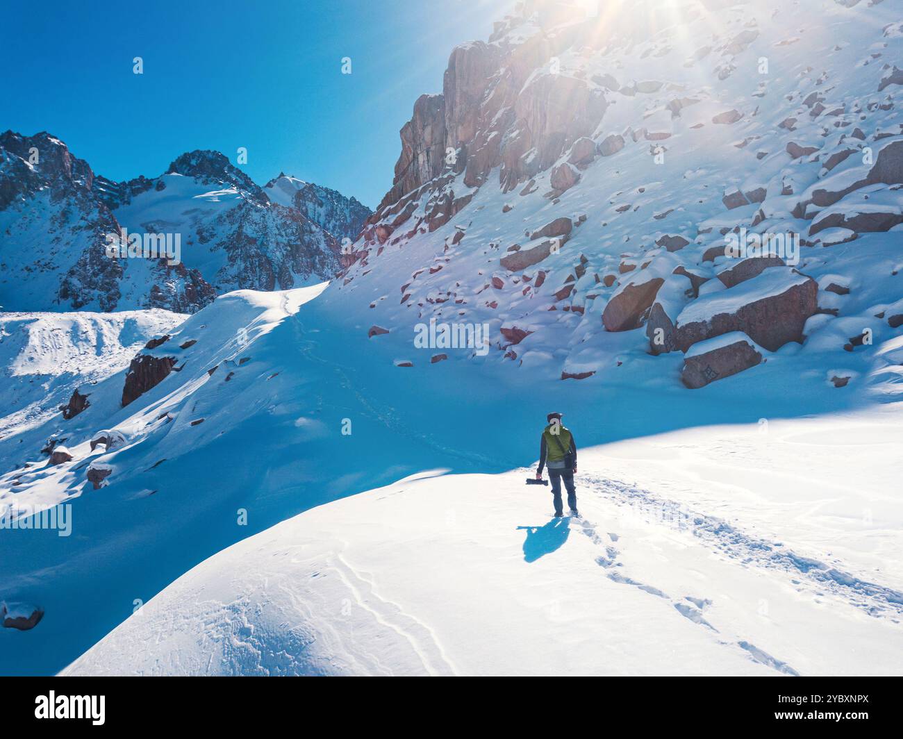 Un uomo con una macchina fotografica in cima alle montagne in una giornata di sole. Il ragazzo ha una fotocamera dotata di un teleobiettivo di grandi dimensioni. Freddo nelle alte montagne. Vie Foto Stock