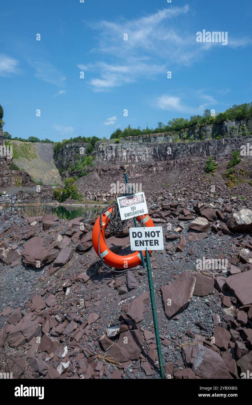 Non entrare e cartello pericolo nessun nuoto avvisano i visitatori di non uscire dall'acqua in una cava di roccia. Un salvagente si aggancia al cartello. Acqua di roccia Foto Stock