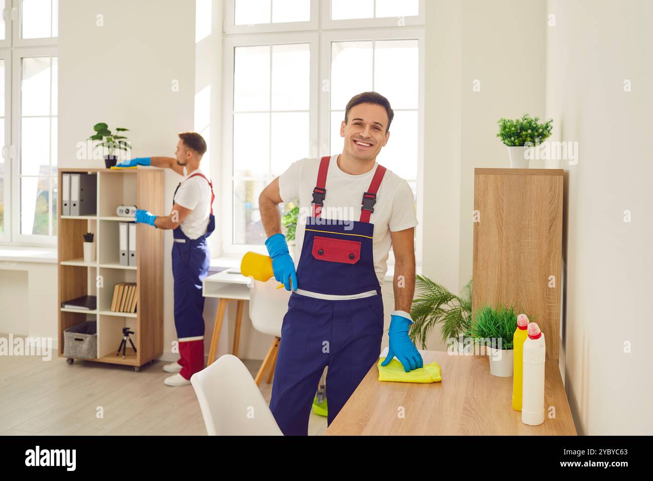 Giovani e felici e sorridenti detergenti maschili in una scrivania con detersivo per la casa. Foto Stock