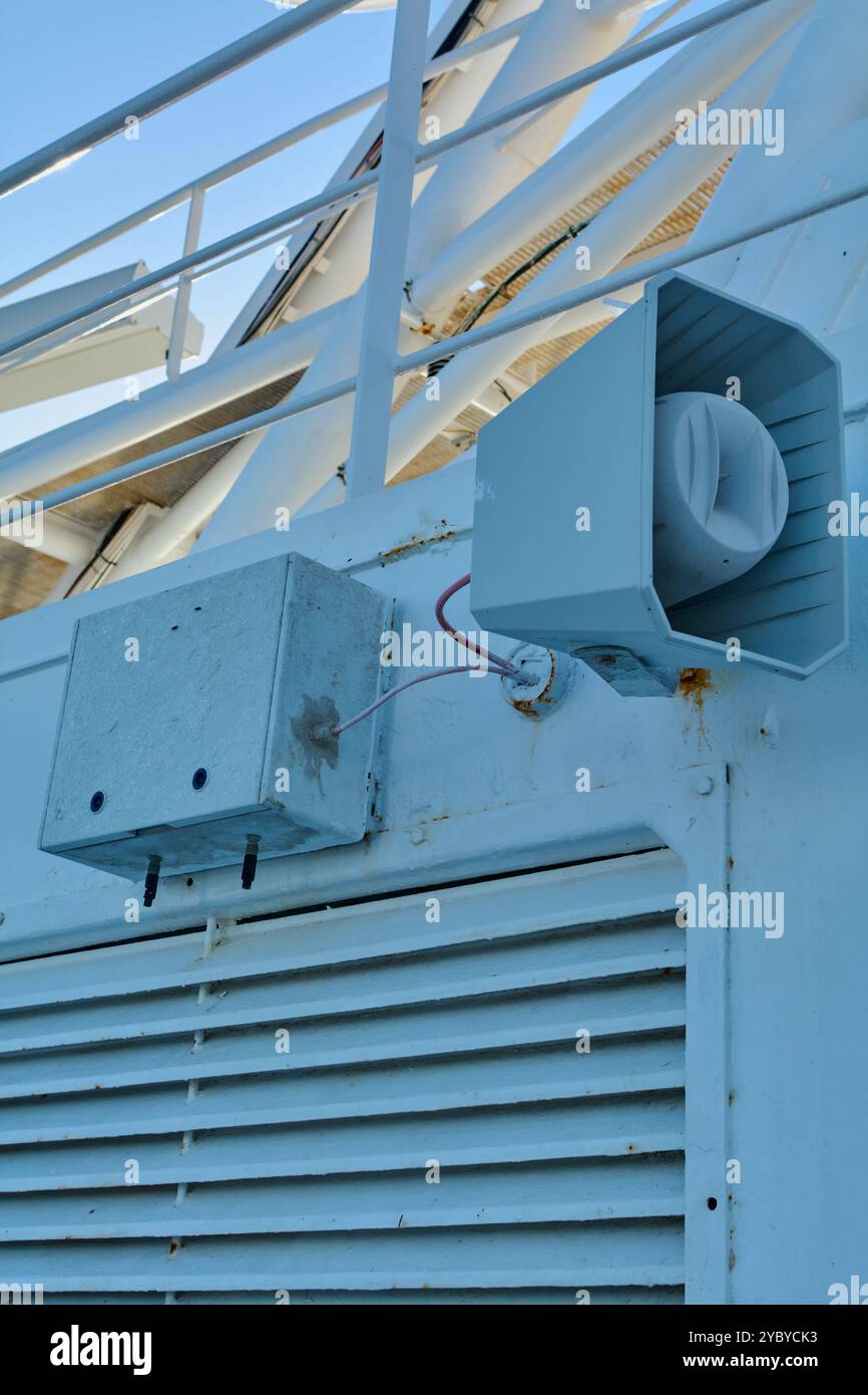 Un sistema di comunicazione pubblica per imbarcazioni montato su una parete grigia, utilizzato per annunci importanti e segnali di emergenza. L'installazione include un altoparlante e un Foto Stock
