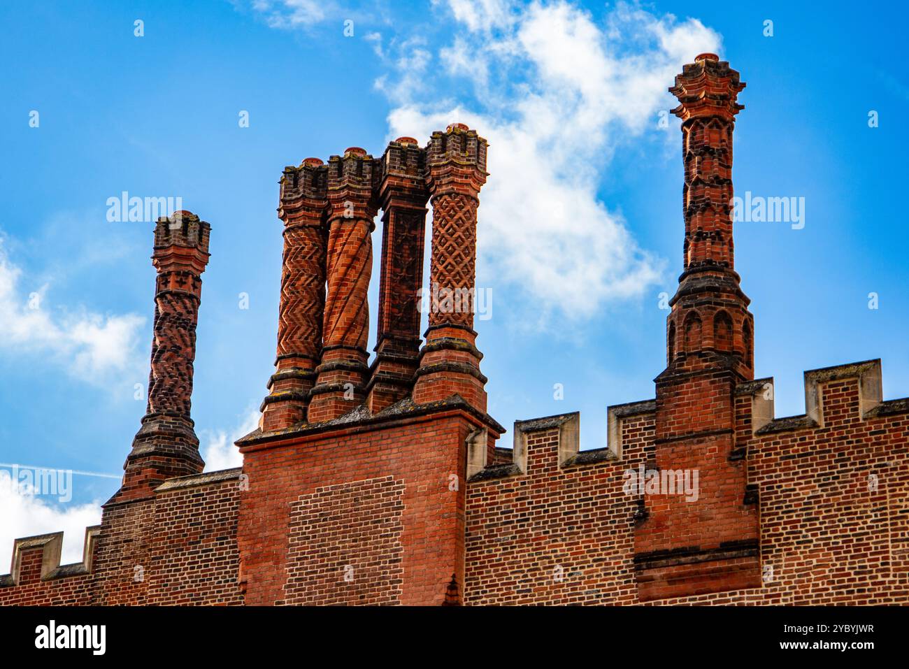 I camini in mattoni Tudor si innalzano contro un vibrante cielo blu con soffici nuvole bianche all'Hampton Court Palace Foto Stock