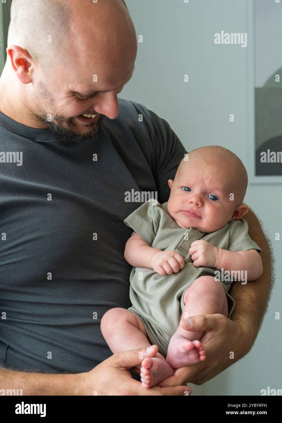 Il padre tiene in braccio il neonato, guardandolo con affetto. Il bambino giace pacificamente tra le braccia del padre. Atmosfera calda e pace. Foto Stock