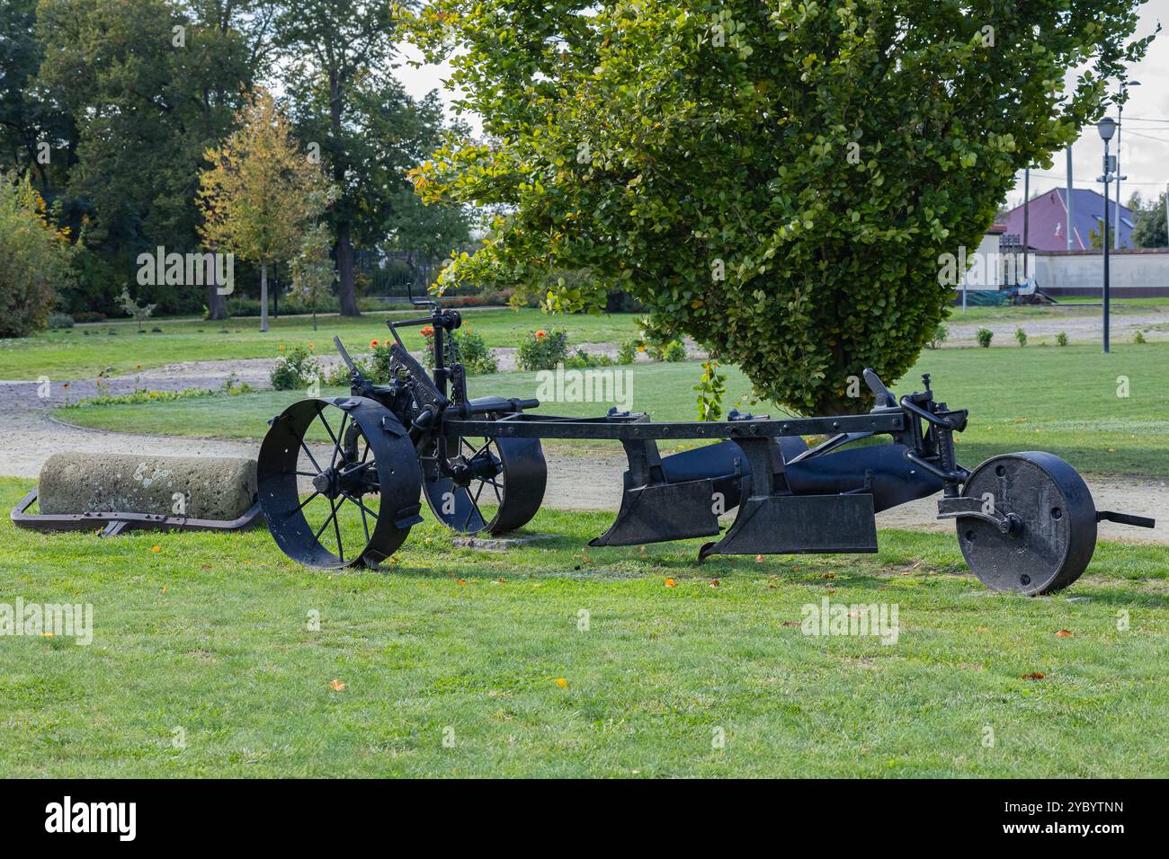 Aratro agricolo d'epoca con grandi ruote esposte su un campo erboso in un parco circondato da alberi in una giornata di sole Foto Stock