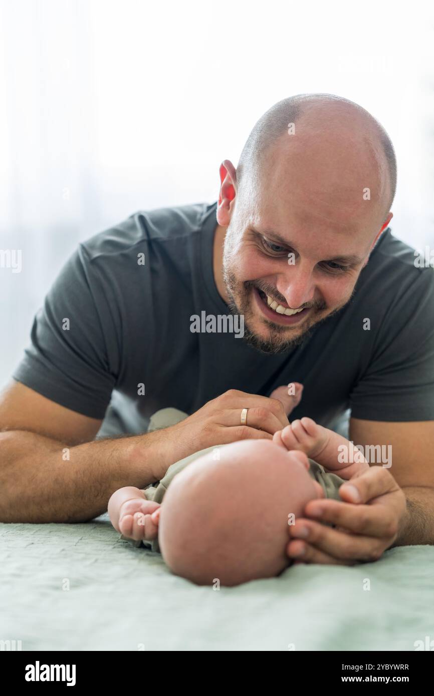 Neonato disteso a letto. Il padre si appoggia sul figlio e guarda delicatamente il bambino. Vicinanza e cura dei momenti toccanti. Uomo amore per figlio Foto Stock