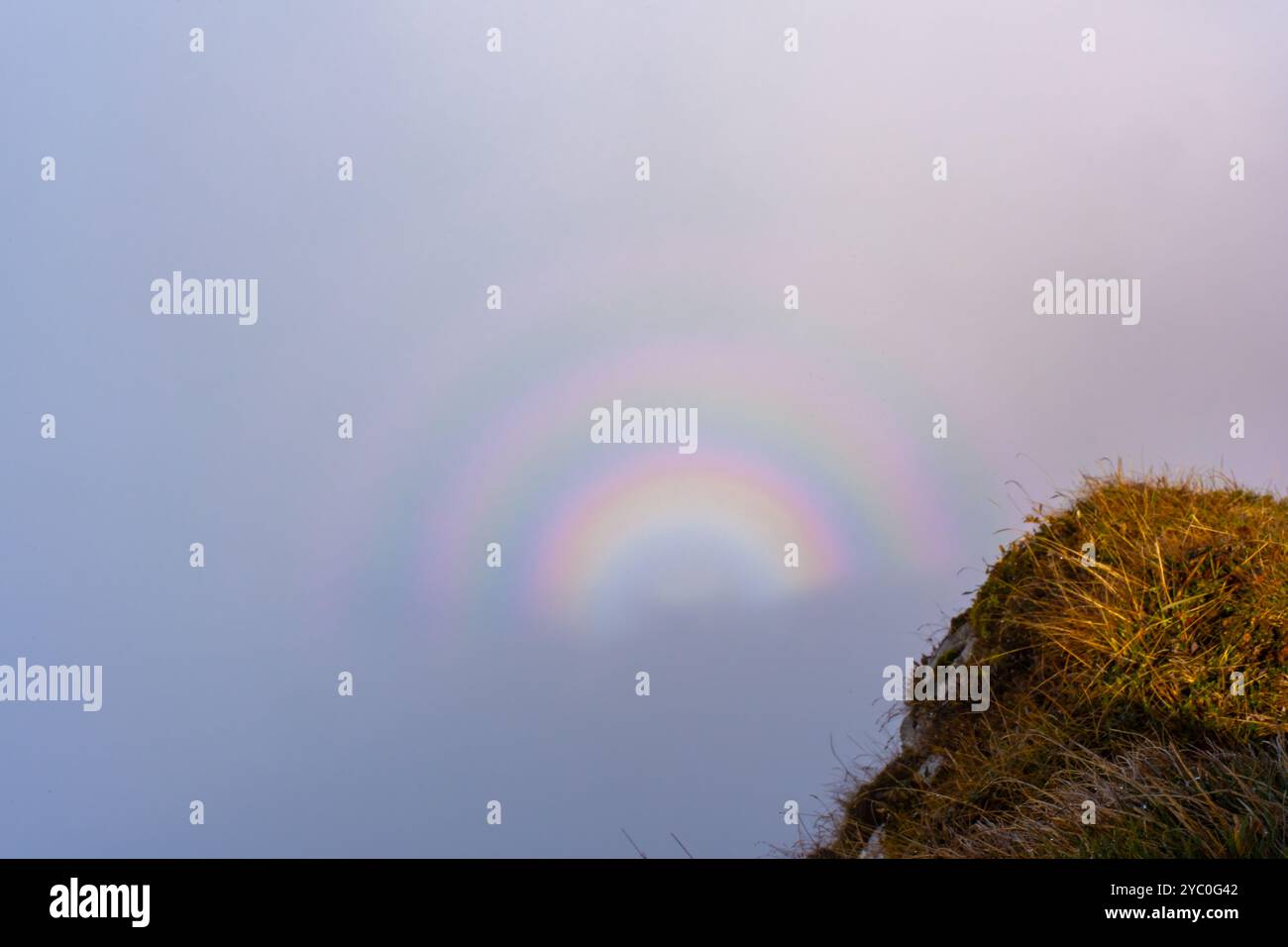 Misteriosa nebbia e arcobaleno su una nuvola sopra una collina erbosa in una mattina nebbiosa. Foto Stock