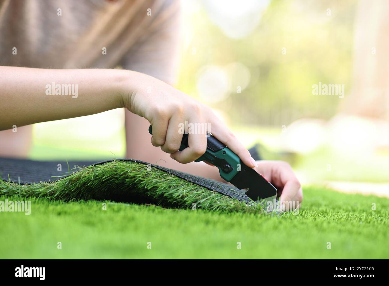 Clos eup di una donna che taglia e installa erba artificiale in un giardino Foto Stock