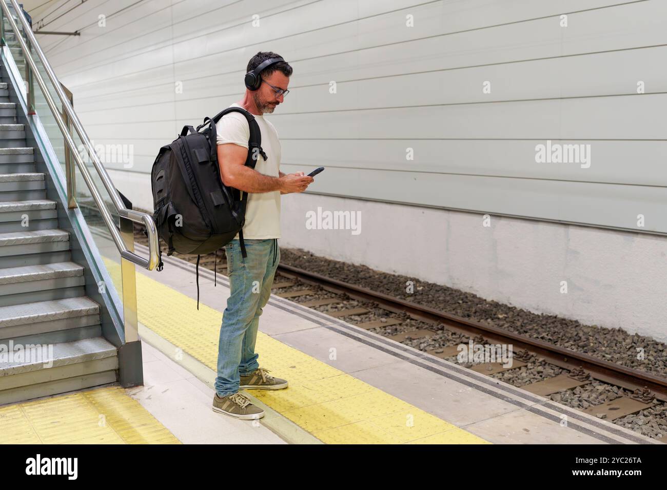 Uomo di mezza età in abbigliamento casual con zaino con smartphone per e-Ticket in attesa del treno in stazione Foto Stock
