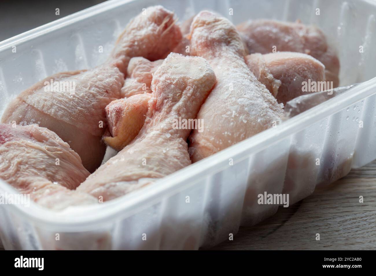 Cosce di pollo surgelate in un contenitore di plastica per scongelare. Su un tagliere di legno Foto Stock