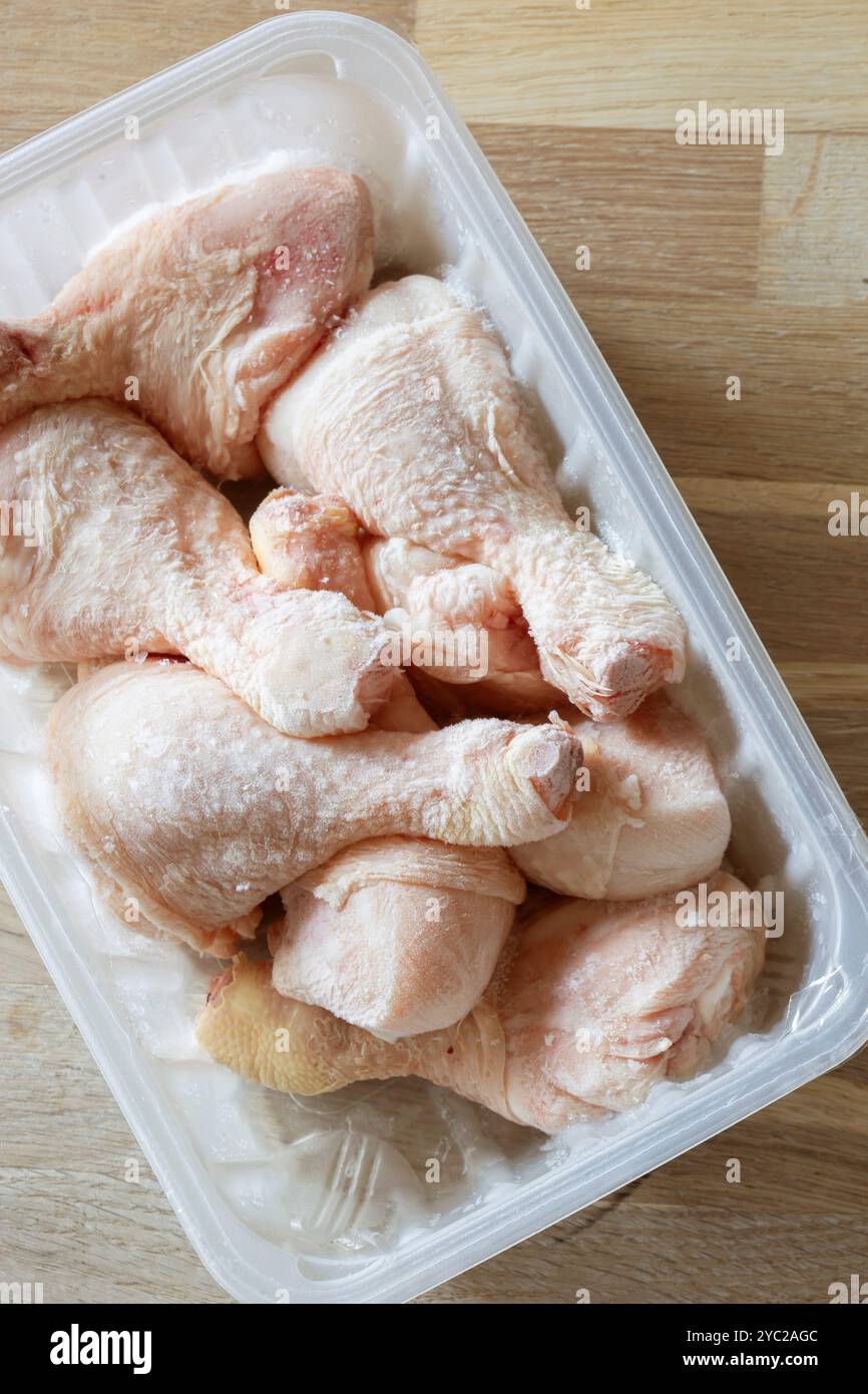 Cosce di pollo surgelate in un contenitore di plastica per scongelare. Su un tagliere di legno Foto Stock