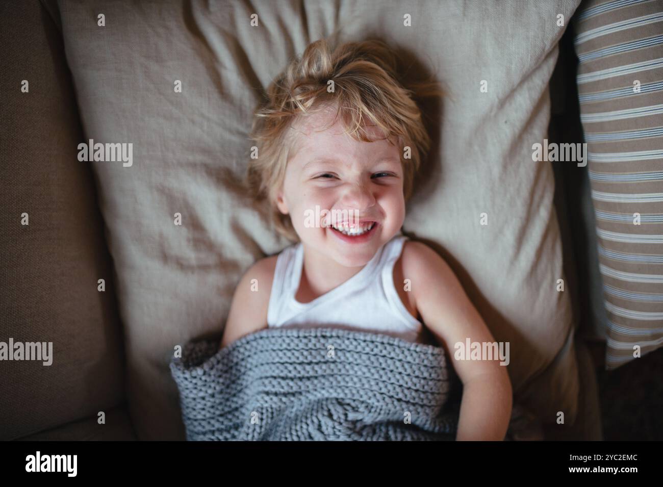Ragazzo malato con febbre e freddo sdraiato sul divano, sotto coperta e sorridente. Foto Stock