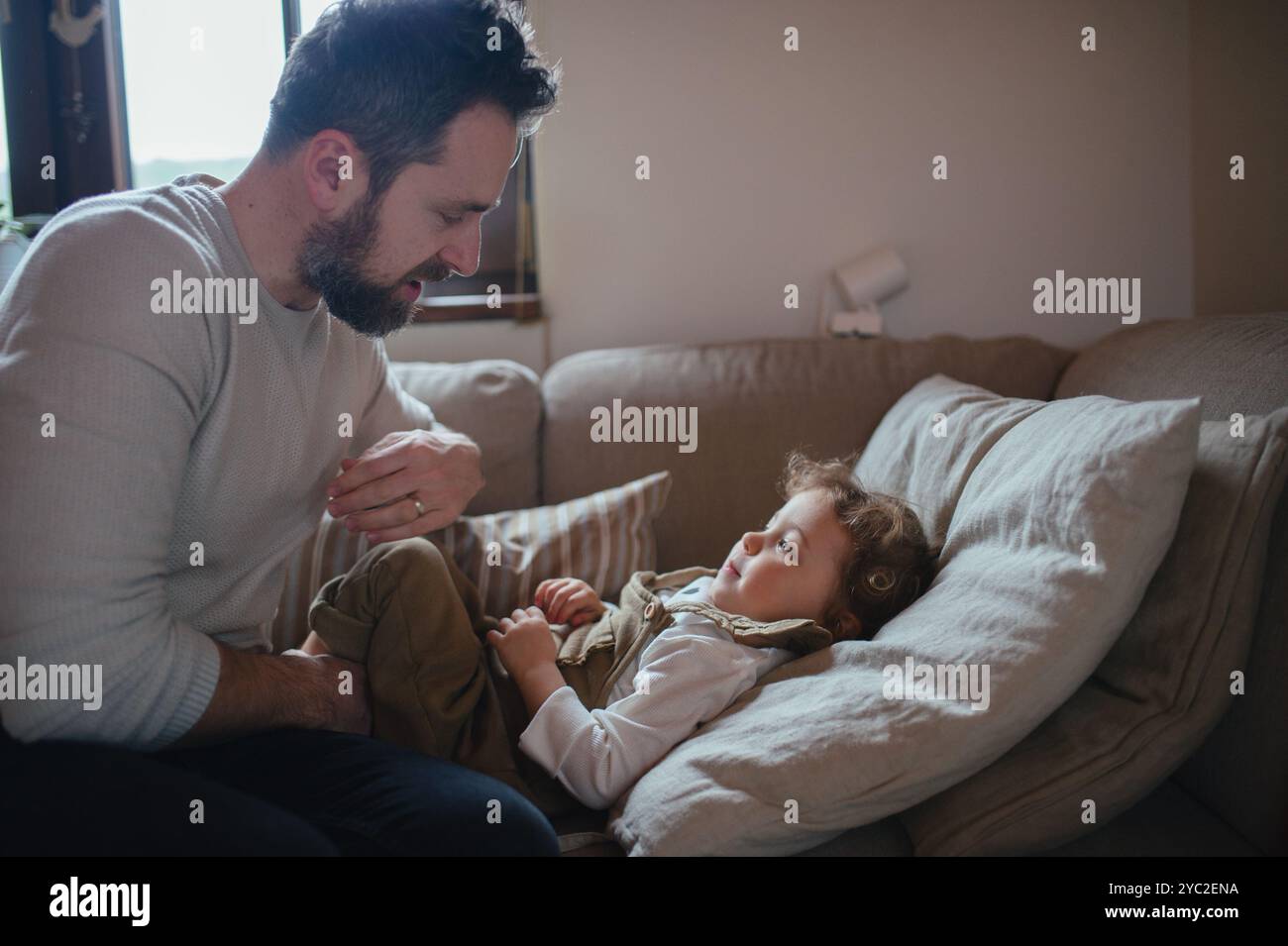 Padre che si prende cura di una ragazza malata con febbre e freddo a casa. Figlia sdraiata sul divano, si sente stanca. Foto Stock