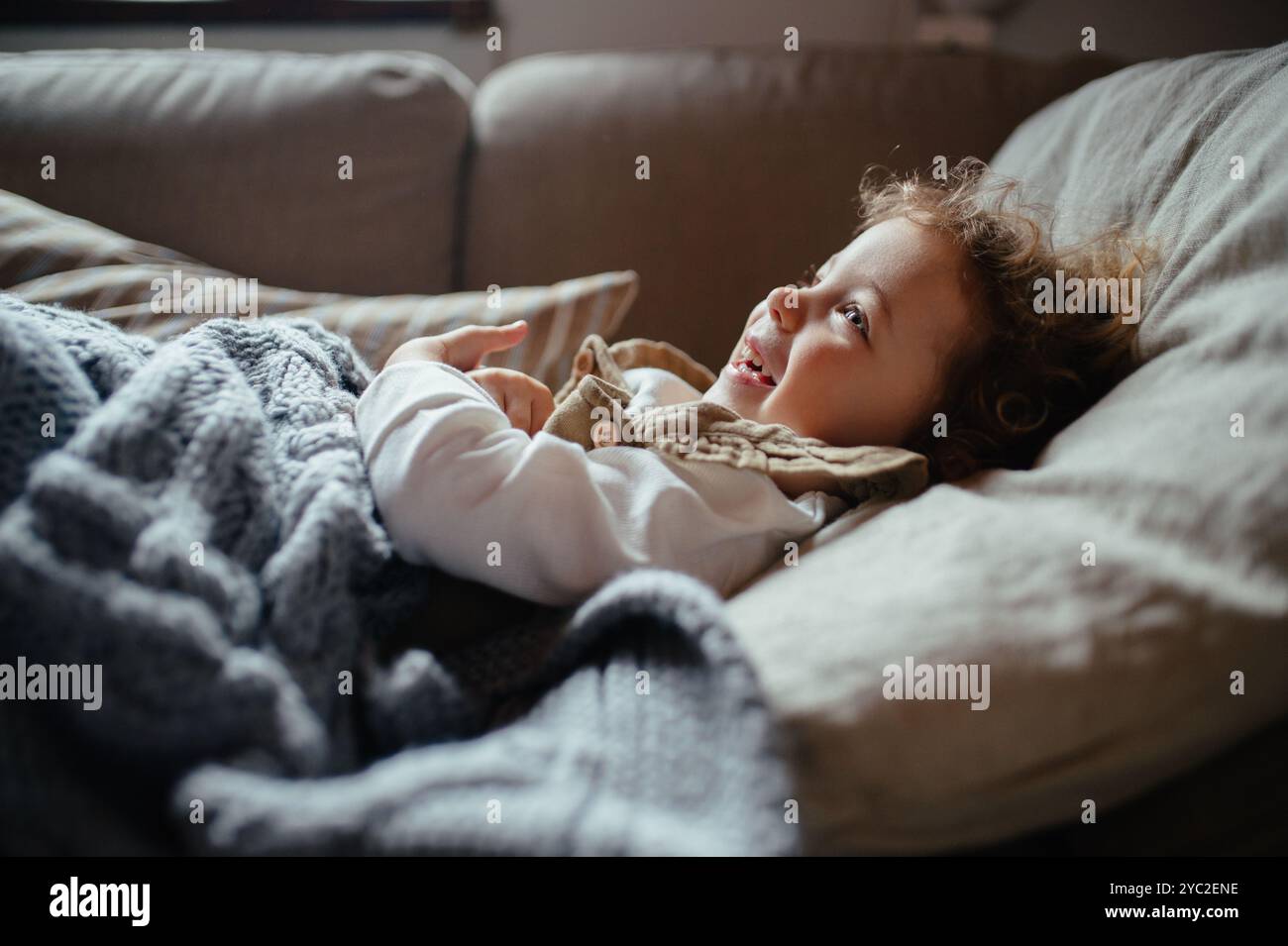 Ragazza malata con febbre e freddo sdraiata sul divano sotto la coperta, sentendosi stanca. Foto Stock