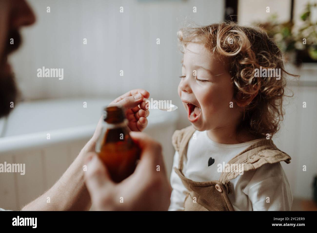 Ragazza malata con febbre e freddo a casa. Padre che dava alla figlia medicine su cucchiaio, sciroppo per tosse o medicina per la febbre. Foto Stock